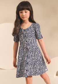 Laivastonsininen kukkamekko, jossa on pöhöttyvät hihat, vaaleanpunaisia ja valkoisia kukkia, pyöreä pääntie ja napit edessä, valmistettu kevyestä kankaasta.