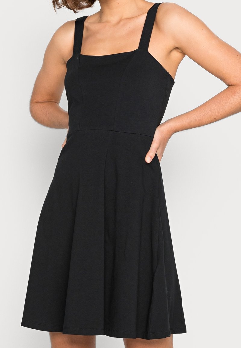 Svart ärmlös klänning med fyrkantig halsringning, figurnära liv och utsvängd kjol. Tillverkad av ett slätt tyg med en ren design och inga mönster.