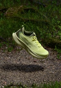 Chaussure de sport vert lime avec un dessus en maillage texturé, semelle rembourrée et logo distinctif, présentée au-dessus d'une surface en gravier.
