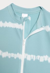 Veste zippée bleu clair avec un tissage texturé, ornée d'un motif ondulé blanc et d'une fermeture éclair blanche contrastante. Col lisse et finitions.