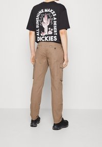 Schwarzes T-Shirt mit kurzen Ärmeln, das weiße grafische Schriftzüge und ein Kaktusdesign auf dem Rücken hat, kombiniert mit hellbraunen Cargo-Hosen mit Seitenstaschen.