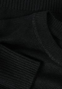 Gros plan sur un tissu noir tricoté montrant des poignets côtelés et un matériau de pull texturé.