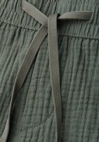 Pantalon en tissu texturé vert olive avec taille élastique et cordon plat noué.