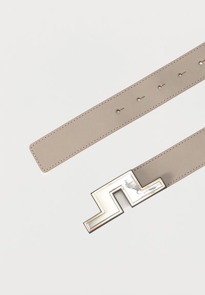 Ζώνη από δέρμα ταουπέ με πολλαπλές τρύπες για ρύθμιση και γυαλιστερή, γωνιώδη, μεταλλική ασημί αγκράφα σε απλό λευκό φόντο.