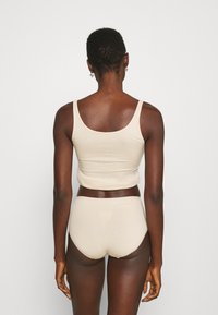 Beige bomulls tanktop og truse sett, med en glatt tekstur, tettsittende design og skulderstropper. Bakfra fremhever den enkelhet.