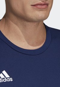 Camiseta de algodón azul marino con cuello redondo, que presenta un logo blanco de Adidas en el lado izquierdo. Textura suave, diseño ajustado.