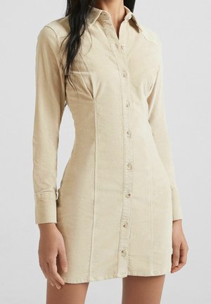 Beige long-sleeve button-up shirt dress with a collar, fitted waist, and soft textured fabric on a standing person.
