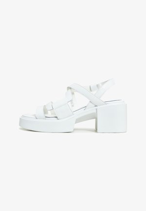 Sandali platform bianchi con tacco a blocco spesso, caratterizzati da cinturini incrociati e una finitura lucida. Design open toe con cuciture minime.