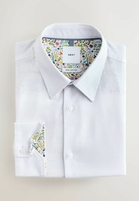 Biała, złożona bawełniana koszula z kwiatowym wzorem na wewnętrznym kołnierzu i mankietach, oznaczona jako "NEXT" i "100% bawełna".