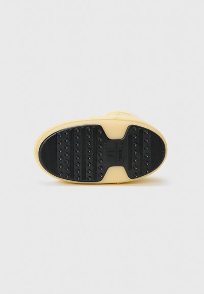 Sole of a yellow shoe with a textured black rubber outsole featuring circular grip patterns and a central logo area.