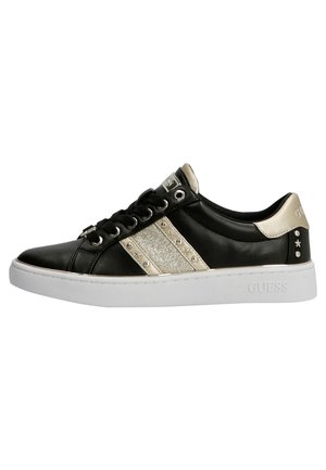 Baskets basses noires avec semelle blanche, bandes latérales dorées pailletées, clous en forme d'étoile, lacets noirs, et languette ainsi que languette du talon en métal doré.