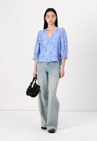 Lys blå blomstermønstret topp med V-hals og ballongslettede ermer, kombinert med lyse denim flared jeans og en liten svart veske.