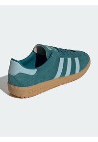 Teal suede sneaker with light blue stripes, gum rubber sole, and textured accents. Features a padded collar and lace-up design.