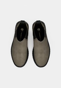 Žemės spalvos slip-on batai su lygia zomšos tekstūra, juodu gumininku ir maža kilpa ant kulno. Timberland logotipas ant vidpadžio.