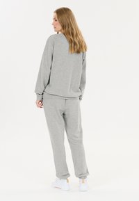 Grå sweatshirt og joggers lavet af blødt bomuldsblandingsmateriale. Sættet har en afslappet pasform, ribbede manchetter og elastisk talje. Hvide sneaks.