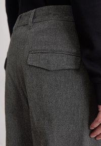 Grijze wollen broek met een gestructureerde afwerking, middelhoge taille en dubbele achterzakken met klepsluitingen. Het ontwerp benadrukt strakke lijnen.