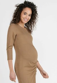 Schwangerschafts Kleid aus einem weichen, braunen Stoff mit einem taillierten Design. Verfügt über Dreiviertelärmel und Raffung an der Seite.