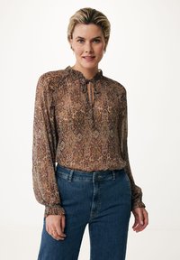 Brun mønstret bluse med flæser ved halsudskæringen, nøglehul-detalje og lange ærmer, parret med blå højtaljede jeans. Subtil tekstur synlig.