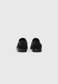 Svarta loafers med texturerat ovandel som har ett subtilt prickmönster, rund tå och en låg, solid svart klack.