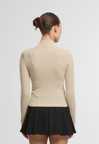 Šviesiai rudos juostelės ilgomis rankovėmis viršus su aukštu apykakle, priderintas prie juodos plisuotos mini sijono. Sklandus paviršius ir minimalus detalizavimas.