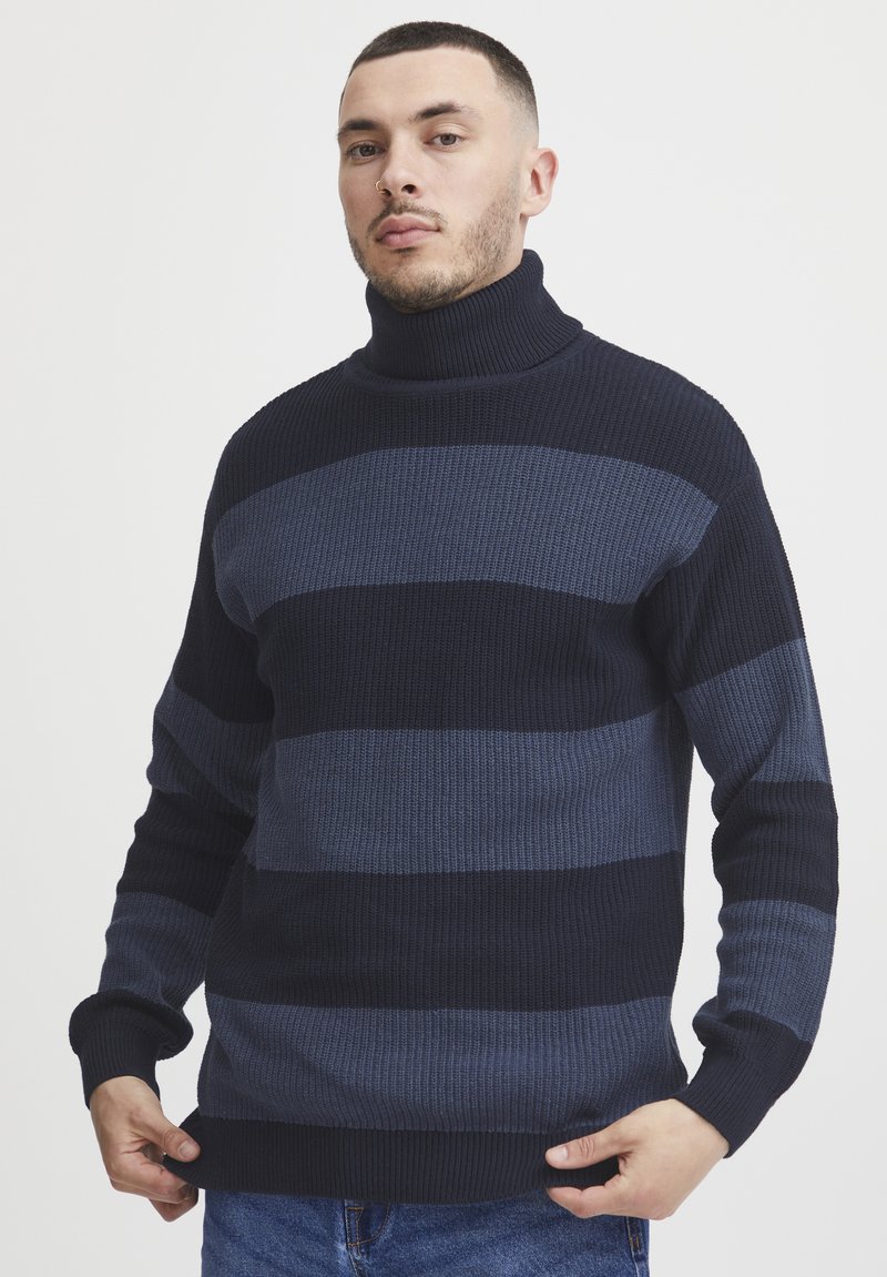 Mornarsko modra in modra prugasta turtleneck pulover iz teksturirane pletenine. Ima dolge rokave in oprijet kroj z rebrastimi manšetami in robom.