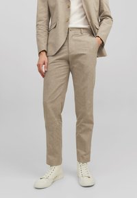 Completo in lino beige con pantaloni slim-fit, caratterizzati da un davanti piatto, una sottile trama e una giacca coordinata. Abbinato a sneakers bianche alte.