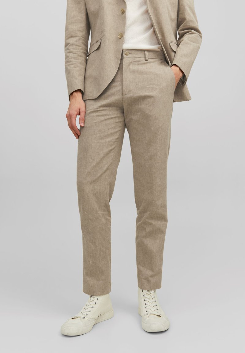 Completo in lino beige con pantaloni slim-fit, caratterizzati da un davanti piatto, una sottile trama e una giacca coordinata. Abbinato a sneakers bianche alte.