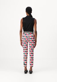 Schwarzes ärmelloses Oberteil, bunte gemusterte Hose mit pinken, grünen und blauen Dreiecken. Taillierte Leoprint-Taille, Slim Fit, cropped Länge. Schwarze Schuhe.