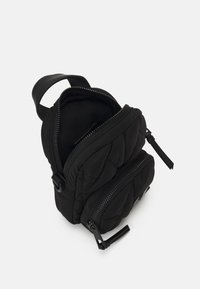 Sort kviltet rygsæk med dobbelte lynlåslommer, blødt strygestof og et robust topgreb. Har minimale hardwaredetaljer.