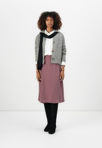 Cardigan grigio lavorato a maglia con dettagli in bottone, camicia bianca e gonna mauve. Stivali neri al ginocchio completano l'outfit. Texture morbide in tutto il look.
