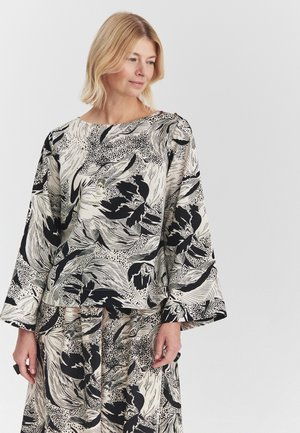 Blonde woman wearing matching black and white floral patterned loose long-sleeve blouse and skirt, looking downward to the right.