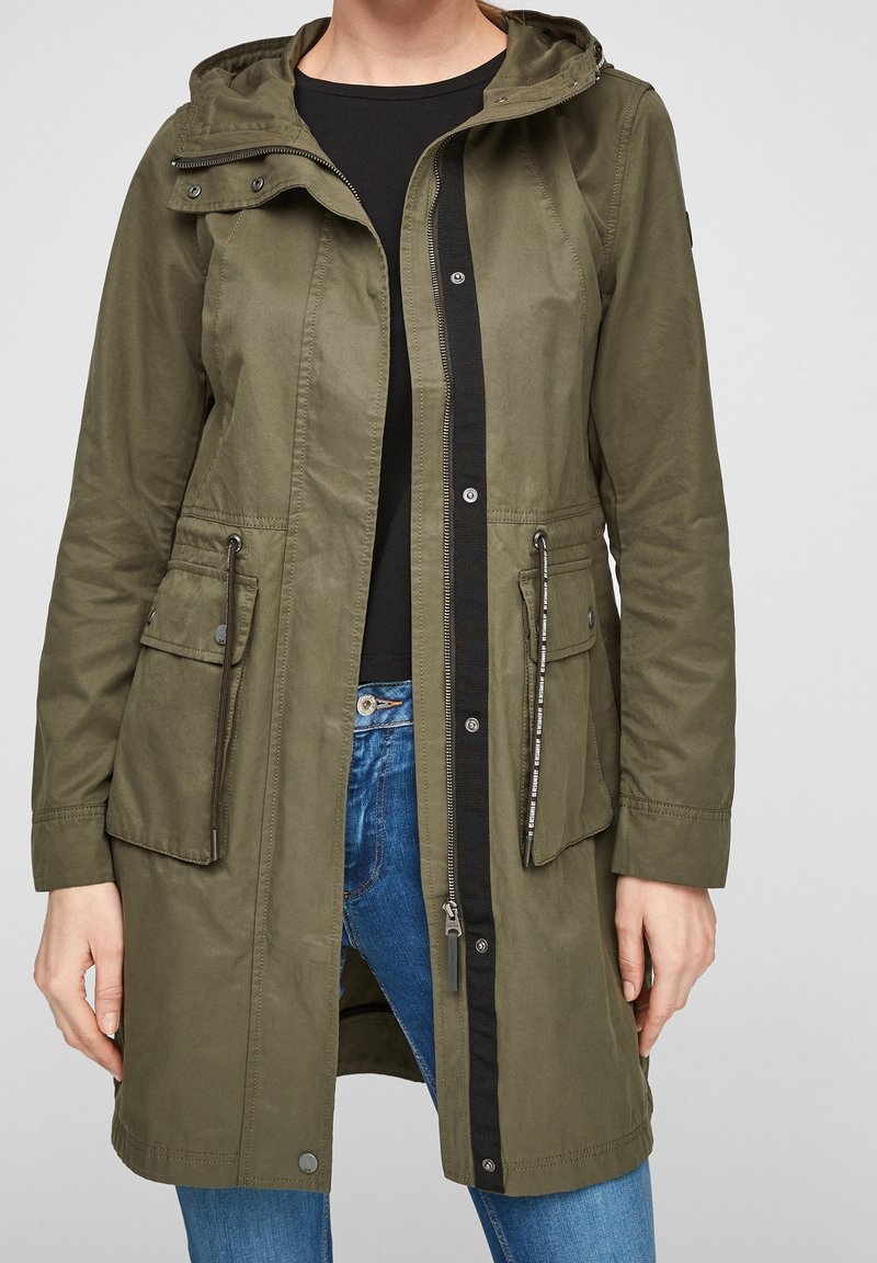 Olive green long jacket, featuring a detachable hood, front zipper, dual side pockets, and drawstring waist detail in a lightweight fabric.