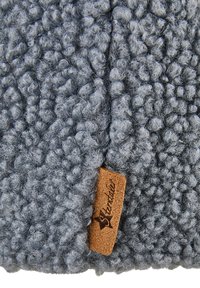 Soft, textured blue-gray knit fabric with a small brown leather tag stitched into the seam, displaying a brand name.