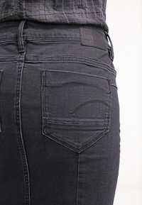 Svarta denimjeans med en texturerad yta, två bakfickor och en läderetikett vid midjan med subtila sömdetaljer.