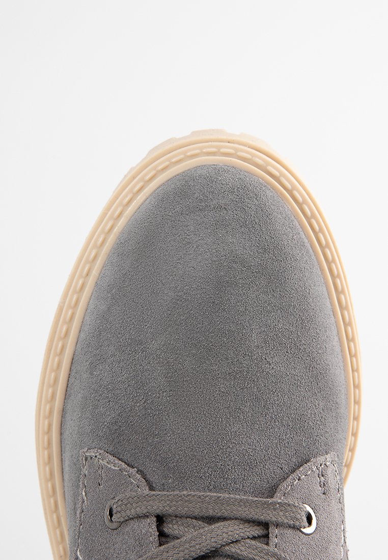 Grauer Wildlederschuh mit beigem Gummisohle und grauen Schnürsenkeln, von oben nah aufgenommen vor einem weißen Hintergrund.