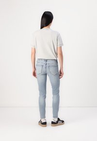 Camiseta gris claro, de mangas cortas, combinada con jeans ajustados azul claro. Zapatillas negras con acentos en blanco y gris. Diseño simple, forma ajustada.