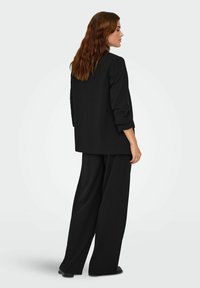 Sort skræddersyet blazer med afslappet pasform, trekvartærmer og brede sorte bukser. Glat stof med et minimalistisk design.