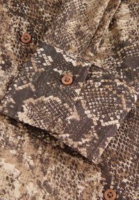 Rudos ir rudos gyvatės rašto audinys su sulenktu rankoviu, papuoštu dviem rudais mygtukais. Texture paviršius su išskirtiniais raštais, primenančiais gyvatės odą.