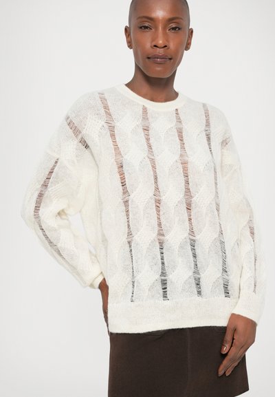 Hvid kabelstrikket sweater med åben vævdesign, rund halsudskæring og lange ærmer, parret med en mørkebrun nederdel.