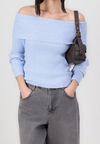 Maglione a coste blu chiaro con spalle scoperte, caratterizzato da maniche lunghe. Abbinato a pantaloni grigi scuri a vestibilità ampia e a una piccola borsa in pelle scura.