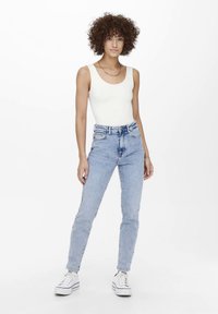 Witte nauwsluitende tanktop gecombineerd met lichtblauwe, high-waisted jeans en witte sneakers. Eenvoudig ontwerp met een gladde textuur en klassieke silhouet.