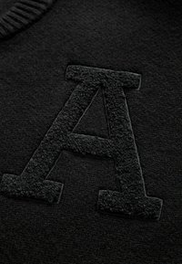 Black fleece fabric featuring a textured, raised letter "A" in a coordinating black color. Ribbed neckline adds detail to the design.