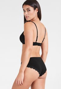 Schwarzes Lingerie-Set mit einem glatten Bralette und dünnen verstellbaren Trägern sowie einem passenden Slip mit Spitzenbesatz an den Kanten.