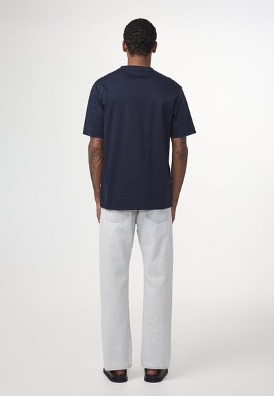 T-shirt navy a maniche corte con colletto tondo, abbinato a jeans dritti grigio chiaro. Il tessuto appare liscio; vestibilità complessiva rilassata.