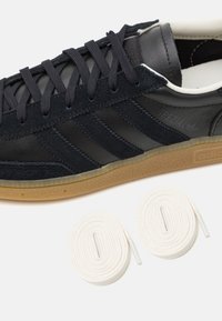 Black leather and suede sneaker featuring three dark blue stripes, a gum sole, and white laces beside the shoe on a light background.