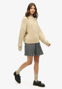 Beige kabelstrik sweater med høj hals, parret med en sort-hvid ternet plisseret nederdel. Båret med sorte loafers og knæhøje strømper.