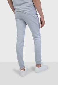 Pantaloni sportivi grigi chiari a sigaretta realizzati in un morbido tessuto, dotati di tasche laterali e polsini elasticizzati, abbinati a sneakers bianche.