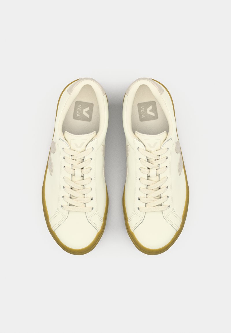 Baskets en cuir couleur crème avec des accents beiges. Les caractéristiques incluent un laçage à l'avant, un bout rond et une semelle en caoutchouc. Marque visible sur les semelles intérieures.