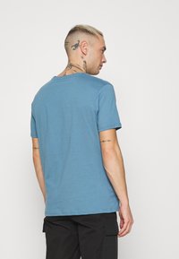 Blaues kurzärmeliges T-Shirt mit klassischem Rundhalsausschnitt und einem weichen, glatten Material, kombiniert mit schwarzen Cargo-Hosen.