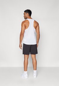 Hvid ærmeløs tanktop med en lav rygdesign, parret med sorte shorts og hvide sneakers. Glat stof, atletisk pasform.